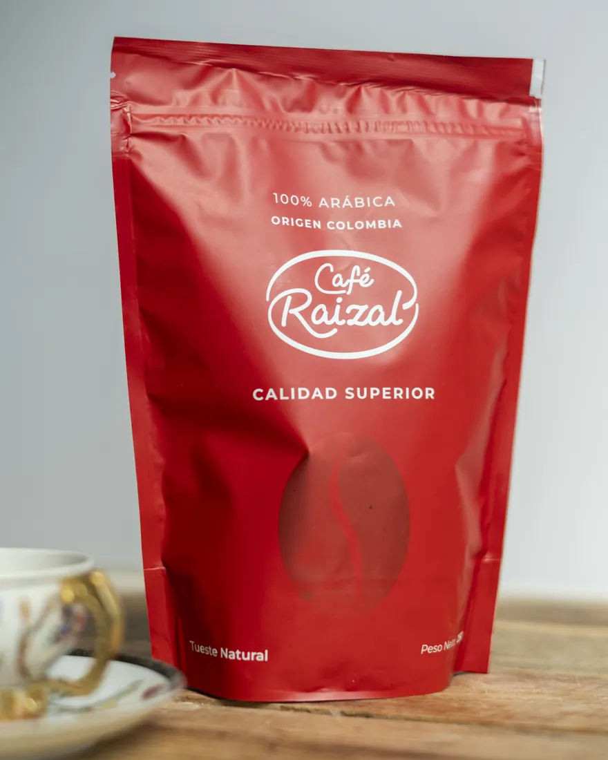 Bolsa roja de Café Raizal junto a una taza de café